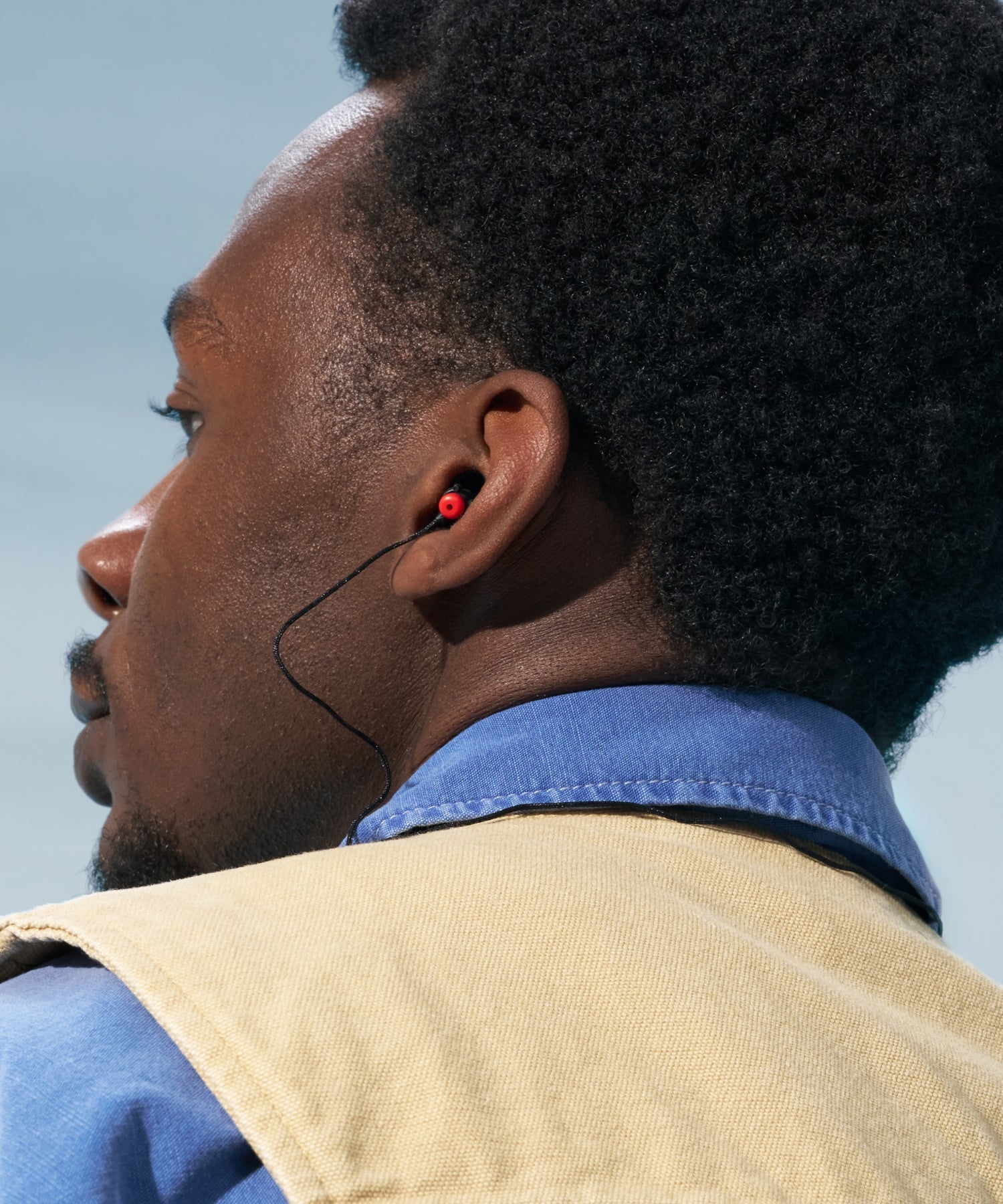 Alpine WorkSafe earplug with black cord worn in the ear by a man in a blue shirt and beige work vest 